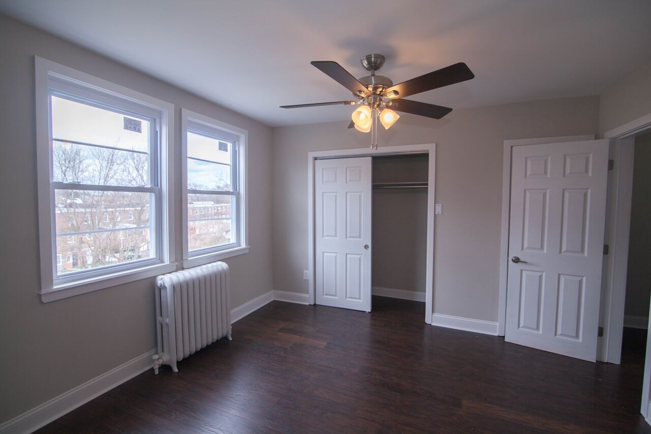 Bright bedroom with two windows, hardwood floors, ceiling fan, and a closet