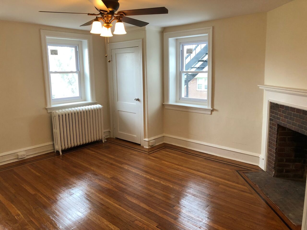 Warm bedroom with two windows, a brick fireplace, and hardwood floors