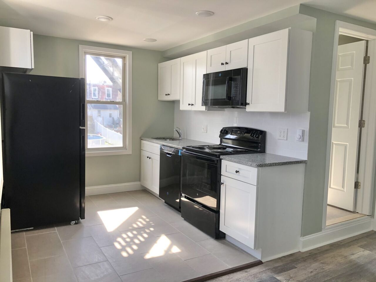 Sunlit renovated kitchen with white shaker cabinets and granite counters
